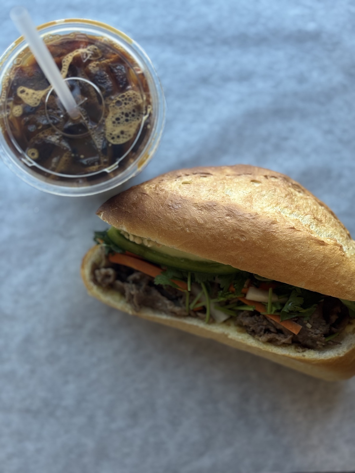 A Crackle & Crumb lemongrass beef banh mi on a fresh-baked baguette next to an iced Vietnamese coffee